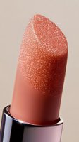Coral pink lipstick with glitter sparkle texture shown in macro detail against neutral background, highlighting shimmering particles and creamy matte finish.