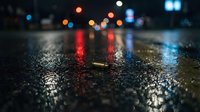 Wet asphalt street at night with colorful bokeh car lights reflecting on rain-soaked pavement, urban nighttime scene for backgrounds and atmospheric designs.