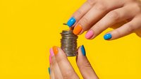 Hands with colorful manicure holding stacked coins against bright yellow background, representing savings, investment, and financial growth for business and money concepts.