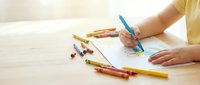 Child drawing with colorful crayons on paper at wooden table. Creative art activity for kids education and development at home or school.
