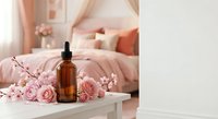 Amber glass dropper bottle with pink roses and cherry blossoms on white surface in cozy bedroom setting for skincare and aromatherapy products.