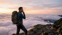 Male hiker with backpack standing on mountain peak above clouds at sunrise, adventure travel and outdoor exploration concept for trekking and mountaineering.