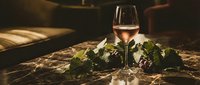 Elegant wine glass filled with rosé wine on rustic wooden table with fresh grape leaves in warm candlelit atmosphere for romantic dining and celebration.