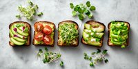 Healthy vegetarian toast variety with avocado, tomatoes, microgreens, and fresh vegetables on dark bread against light background.
