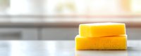 Stack of bright yellow cleaning sponges on white surface in modern kitchen interior with soft natural lighting for household maintenance tasks.