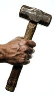 Weathered hand gripping vintage wooden sledgehammer with worn metal head isolated on white background for construction and labor concepts.