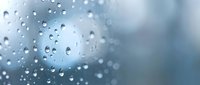 Water droplets on glass surface with soft blue background creating peaceful rainy day atmosphere for relaxation and mindfulness concepts.