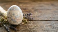 Hand-painted Easter egg with delicate floral patterns sits on rustic wooden background with dried lavender sprigs and moss for spring holiday decorations.