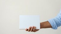 Male hand holding blank white card or envelope against neutral background for mockup and branding purposes.