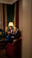 Elegant couple enjoying drinks in luxury hotel lounge with warm lighting and rich velvet curtains creating romantic atmosphere for special occasion.
