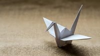 White origami crane on rustic burlap background, symbol of peace, hope and Japanese art tradition, perfect for cultural and mindfulness projects.