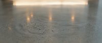 Wet concrete floor with water droplets and warm light reflections creating atmospheric industrial interior surface for modern architecture projects.