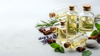 Essential oils in glass bottles with cork stoppers, fresh herbs, lavender, mint leaves and cinnamon sticks on white textured background for aromatherapy.