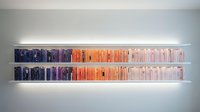 Modern floating bookshelf with color-coordinated books arranged from dark blue to orange to white creating gradient effect on minimalist white wall.