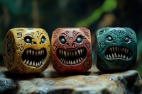 Whimsical monster dice with sharp teeth and expressive eyes in yellow, red, and turquoise colors, featuring decorative swirl patterns on textured surface against dark background.