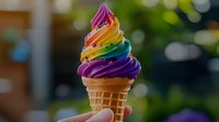 Rainbow swirled soft serve ice cream cone held against blurred natural background, featuring vibrant colors from purple to pink with sprinkles on top.