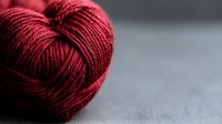 Close-up of deep burgundy yarn skein on gray textured surface, showcasing rich color and twisted fiber detail for knitting and crochet projects.