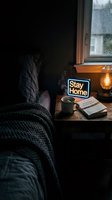 Cozy dark bedroom with neon stay home sign, steaming coffee cup, vintage lamp, and open book on wooden nightstand by rainy window.