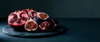 Fresh pomegranate and figs sliced on dark slate board, moody food photography with rich red tones and dramatic dark background.