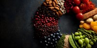 Colorful circular arrangement of superfoods, spices, nuts, berries, and vegetables on dark background, showcasing rainbow of nutritious ingredients for healthy eating.
