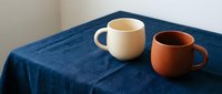 Two ceramic coffee mugs on blue linen tablecloth creating cozy morning atmosphere for kitchen decor and beverage photography.