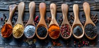 Colorful ground spices and seasonings in wooden spoons arranged in row on dark rustic background, variety of cooking ingredients for food preparation.