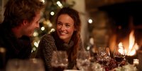 Young woman smiling during festive dinner with friends, enjoying wine by fireplace and Christmas tree lights in cozy home atmosphere.