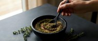 Hand stirring aromatic herbs and spices in black bowl on kitchen counter. Culinary preparation with fresh thyme for cooking and seasoning recipes.