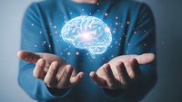 Person in blue shirt holding glowing brain hologram with sparkling light effects representing artificial intelligence, neuroscience and mental health concepts.