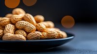 Fresh roasted peanuts in shell on dark plate with soft bokeh lights in background, macro food photography with selective focus and warm tones.
