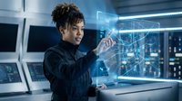 Young female engineer with curly dark hair and medium brown skin tone interacting with holographic data visualization in high-tech laboratory setting for technology and innovation concepts.