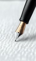 Gold fountain pen nib with ornate engraving shown in macro detail against white textured paper background, highlighting craftsmanship and writing precision.