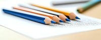 Colored pencils lying on white paper with delicate sketch marks, shallow depth of field creates artistic composition for creative and educational concepts.