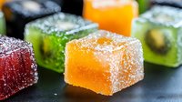 Colorful fruit jelly cubes covered in sugar crystals on dark background, macro shot showing texture and sparkle. Sweet treats with orange, green and red colors.