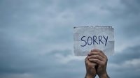 Hands holding cardboard sign with sorry message against cloudy sky background expressing apology regret forgiveness concept for emotional communication.