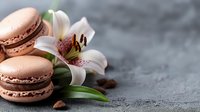 Pink macarons with white lily flower and coffee beans on dark concrete background, elegant food composition for pastry shop advertising.