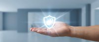 Male hand holding glowing shield security icon in modern office environment, representing data protection, cybersecurity solutions, and digital safety technology for business applications.