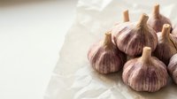 Fresh garlic bulbs with papery skin arranged on white crumpled paper, suitable for cooking, food photography, culinary content, and recipe illustrations.