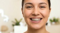 Happy young Hispanic woman with metal braces smiling at camera in modern dental office, showing orthodontic treatment progress for oral health care.