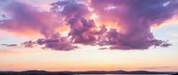 Dramatic purple and pink sunset clouds over mountain silhouettes and calm water creating stunning twilight sky reflection for nature backgrounds.