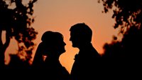 Romantic couple silhouettes facing each other at sunset with tree branches framing the scene, creating intimate moment for wedding and love concepts.