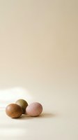 Three speckled Easter eggs in muted earth tones rest on a beige surface with soft natural light and copy space above.