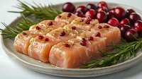 Raw salmon pieces garnished with pink peppercorns, sea salt, and fresh rosemary on ceramic plate, served with fresh cranberries for festive dining.