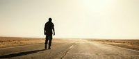 Lone traveler walking on empty desert highway at sunset with golden light and endless horizon for adventure and freedom concepts.