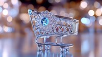 Decorative shopping cart made of silver metal wire with blue gemstone ornament on blurred bokeh background. Miniature artistic retail symbol.