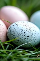 Speckled pastel eggs nestled in fresh green grass, with soft focus creating dreamy spring atmosphere. Close-up macro photography shows delicate spotted patterns.