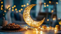 Glowing decorative crescent moon with warm string lights and traditional dates on wooden surface against blurred bokeh background creates Ramadan atmosphere.