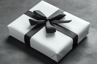 White gift box wrapped with black satin ribbon bow on dark background. Elegant monochrome composition for special occasions and holiday presents.