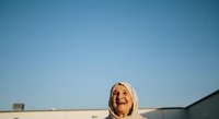 Mature blonde woman smiling outdoors against clear blue sky and industrial rooftop background, suitable for business, lifestyle, and corporate marketing materials.