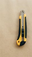 Yellow utility knife with retractable blade on cardboard surface for crafting and office work projects.